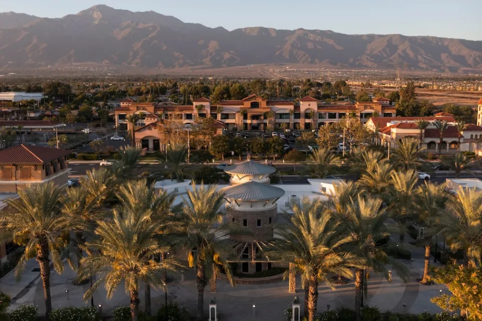 Aerial view of Rancho Cucamonga, California with suburban commercial center and large palm trees at sunset with mountains in background.